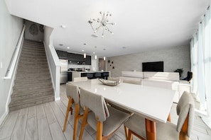 A modern kitchen with a central island, a dining area with a large table and chairs, and a staircase leading to an upper level.