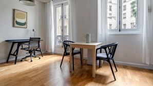 A modern room with a wooden floor, a desk with a chair, a table with two chairs, and large windows with curtains. - Blueground | Champs Elysees, nr Arc de Triomphe (Paris)