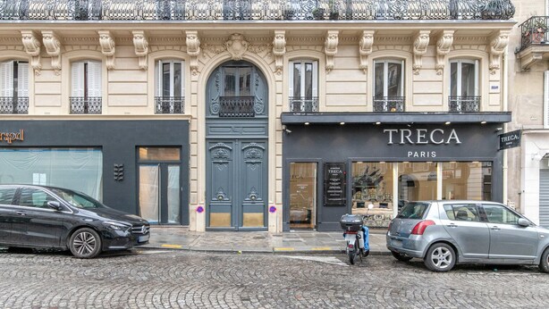 A cobblestone street with parked cars and a building featuring a large, ornate door and windows. - Blueground | Champs Elysees, nr Arc de Triomphe (Paris)