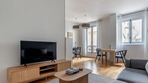 A modern living room with a flat-screen TV, wooden furniture, a dining area, and large windows. - Blueground | Champs Elysees, nr Arc de Triomphe (Paris)