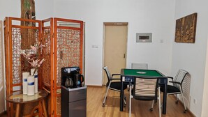 Une pièce de taille modeste, comprenant une table basse en bois, un petit réfrigérateur, un billard vert et un paravent décoratif orné de motifs floraux.