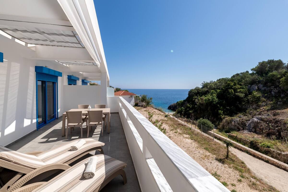 A balcony with lounge chairs and a table overlooking the sea.