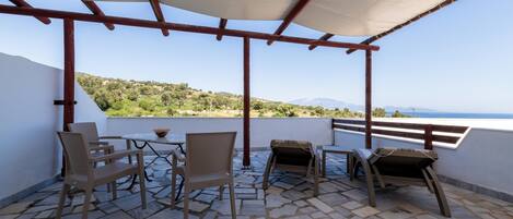 A terrace with stone flooring, wicker furniture, and a view of the sea.