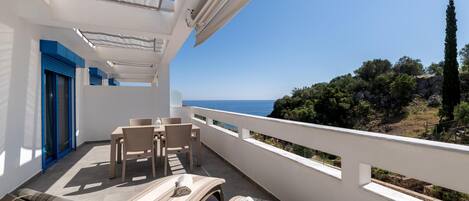 A balcony with a view of the sea, a table with chairs, and a sun lounger.
