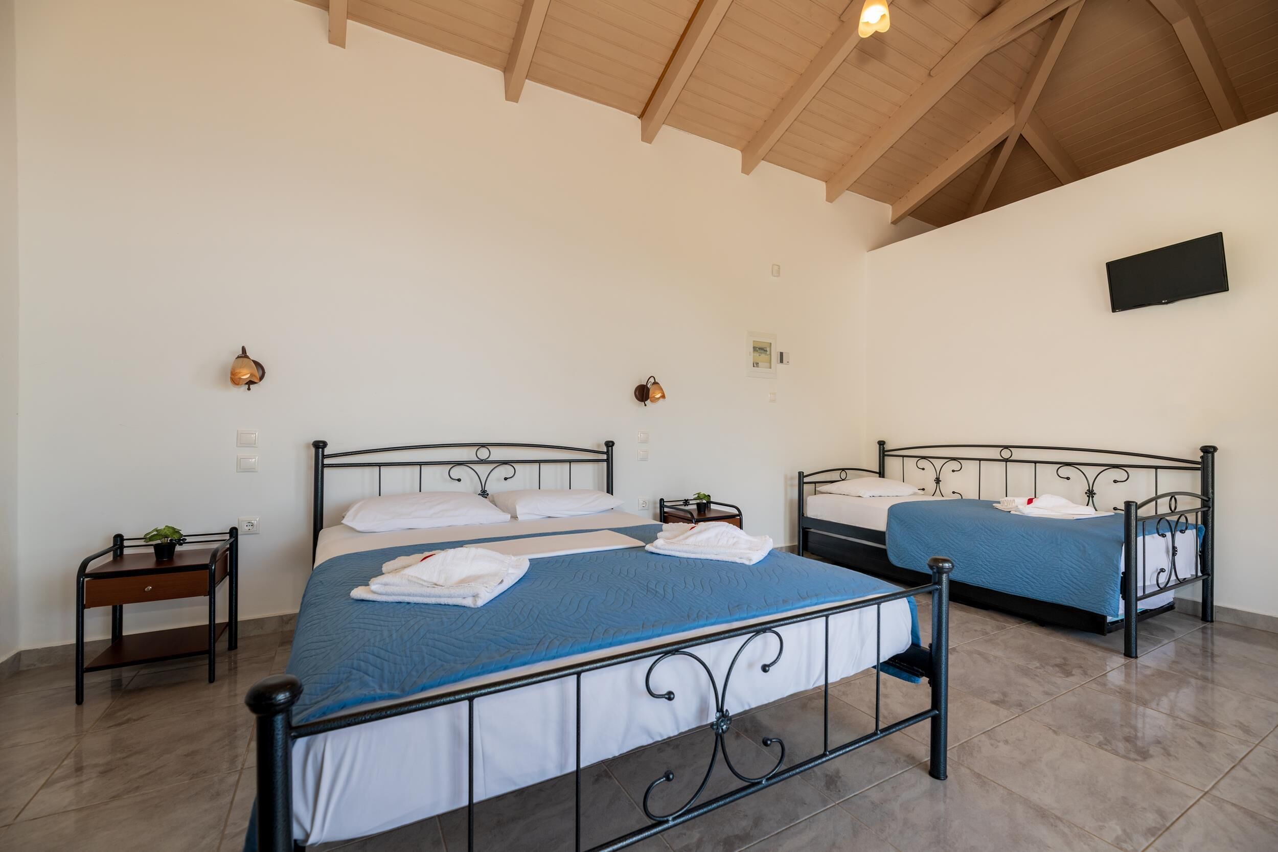 A bedroom with two beds, a TV mounted on the wall, and a ceiling with wooden beams.