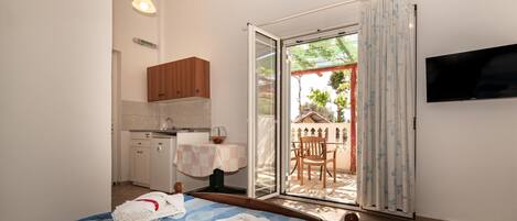 A hotel room with a bed, a TV, a kitchenette, and a sliding glass door to an outdoor area with a table and chairs.