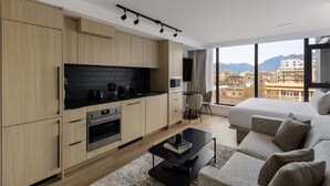 A modern hotel room with a kitchen, a large bed, and a city view. - Keefer House (Vancouver)