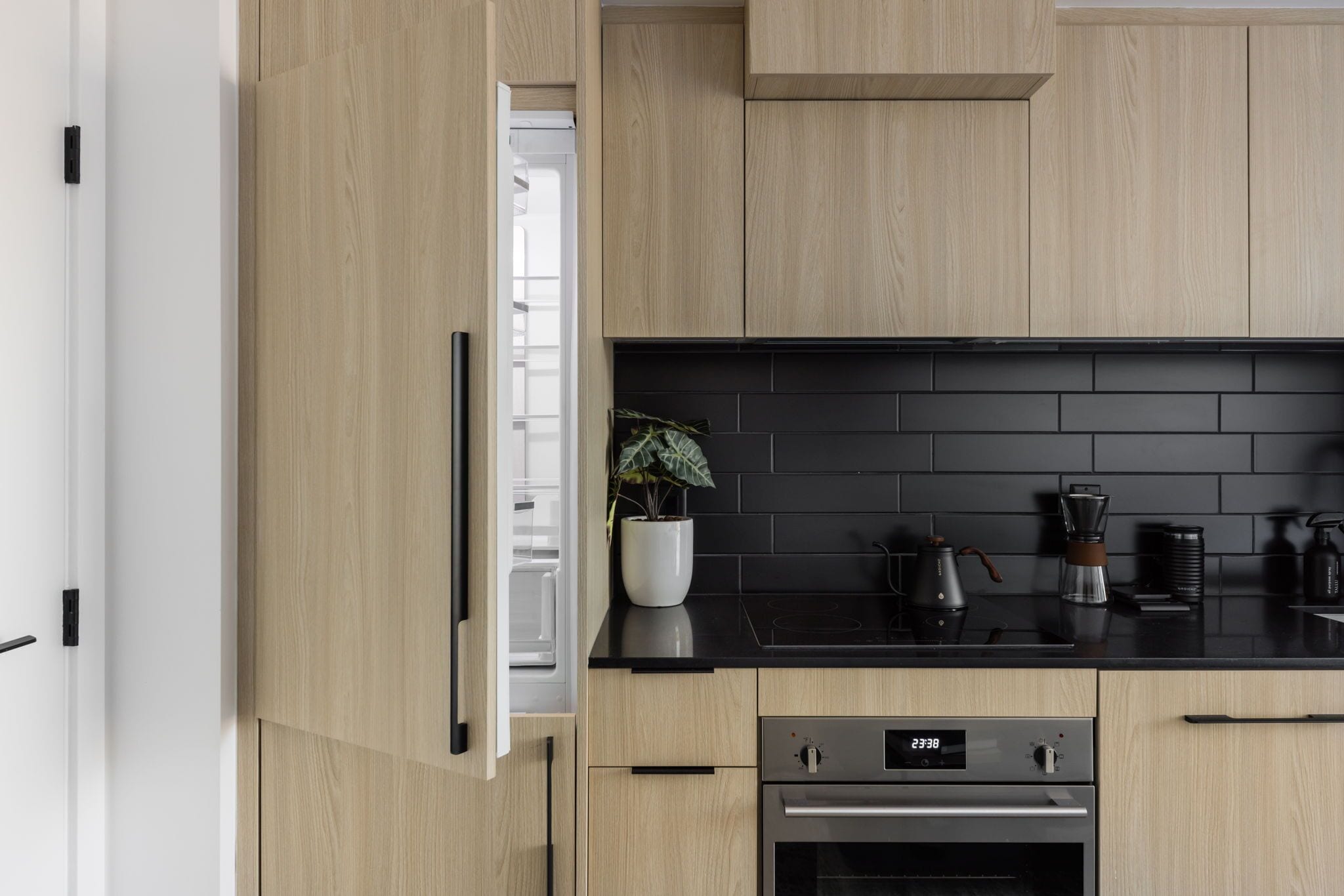 Una cocina moderna con armarios de madera, encimera negra, cafetera y un reloj digital que marca las 23:38.