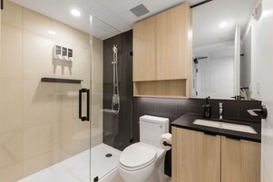 Un baño moderno con cabina de ducha de vidrio, inodoro, lavabo con encimera negra y armarios de madera.