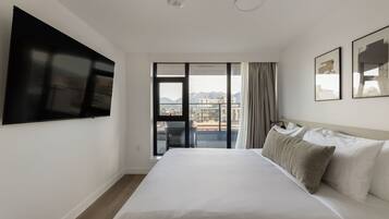 A hotel room with a large bed, a flat-screen TV mounted on the wall, and a balcony with a city view.