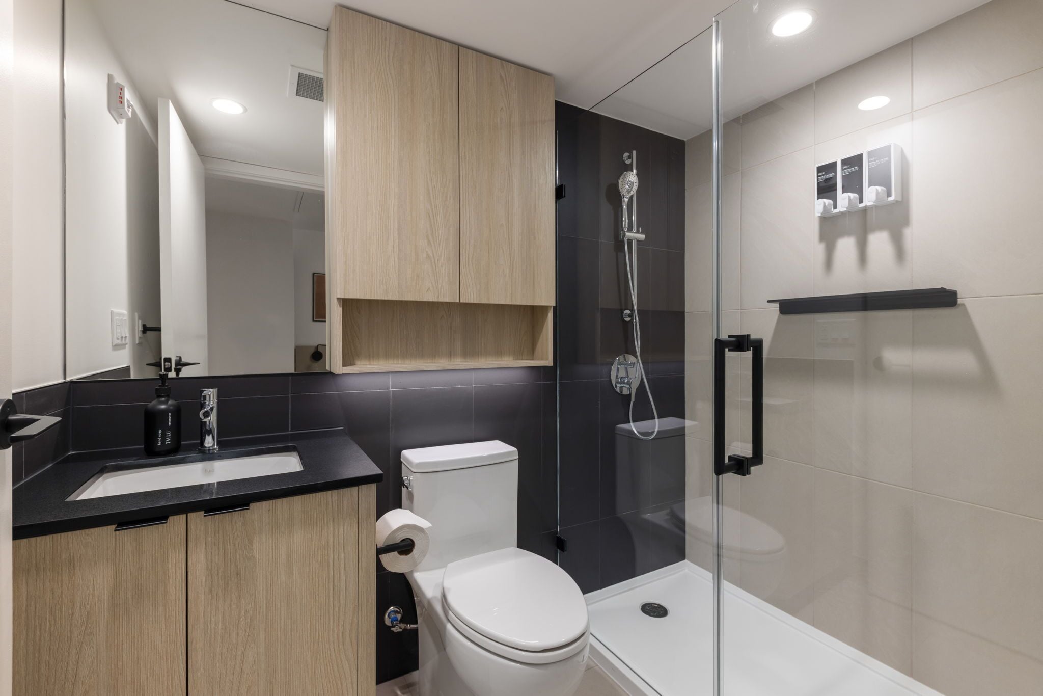 A modern bathroom with a glass-enclosed shower, a white toilet, and a wooden vanity with a black countertop.