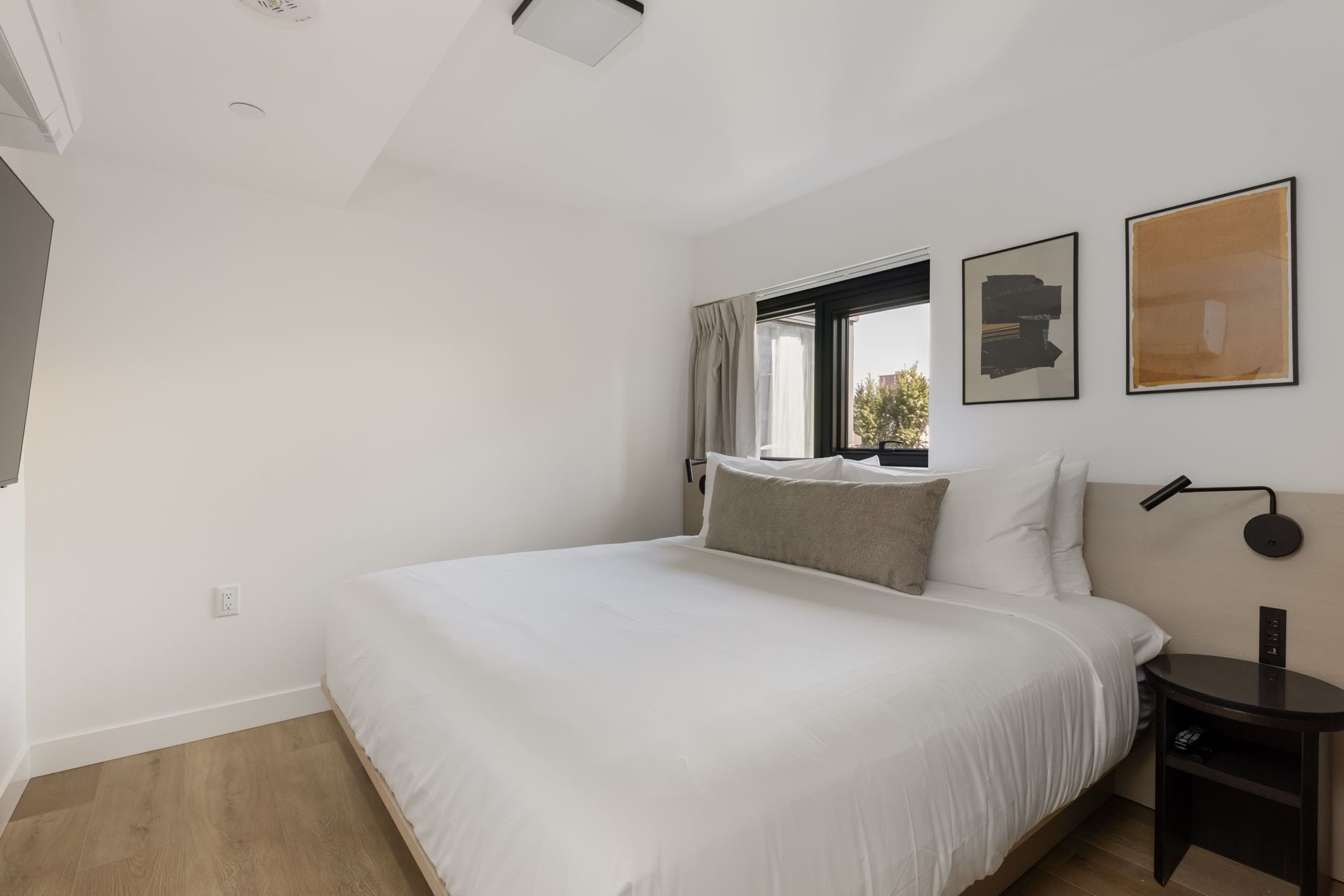 A modern hotel room with a large bed, a bedside table, a lamp, and artwork on the wall.