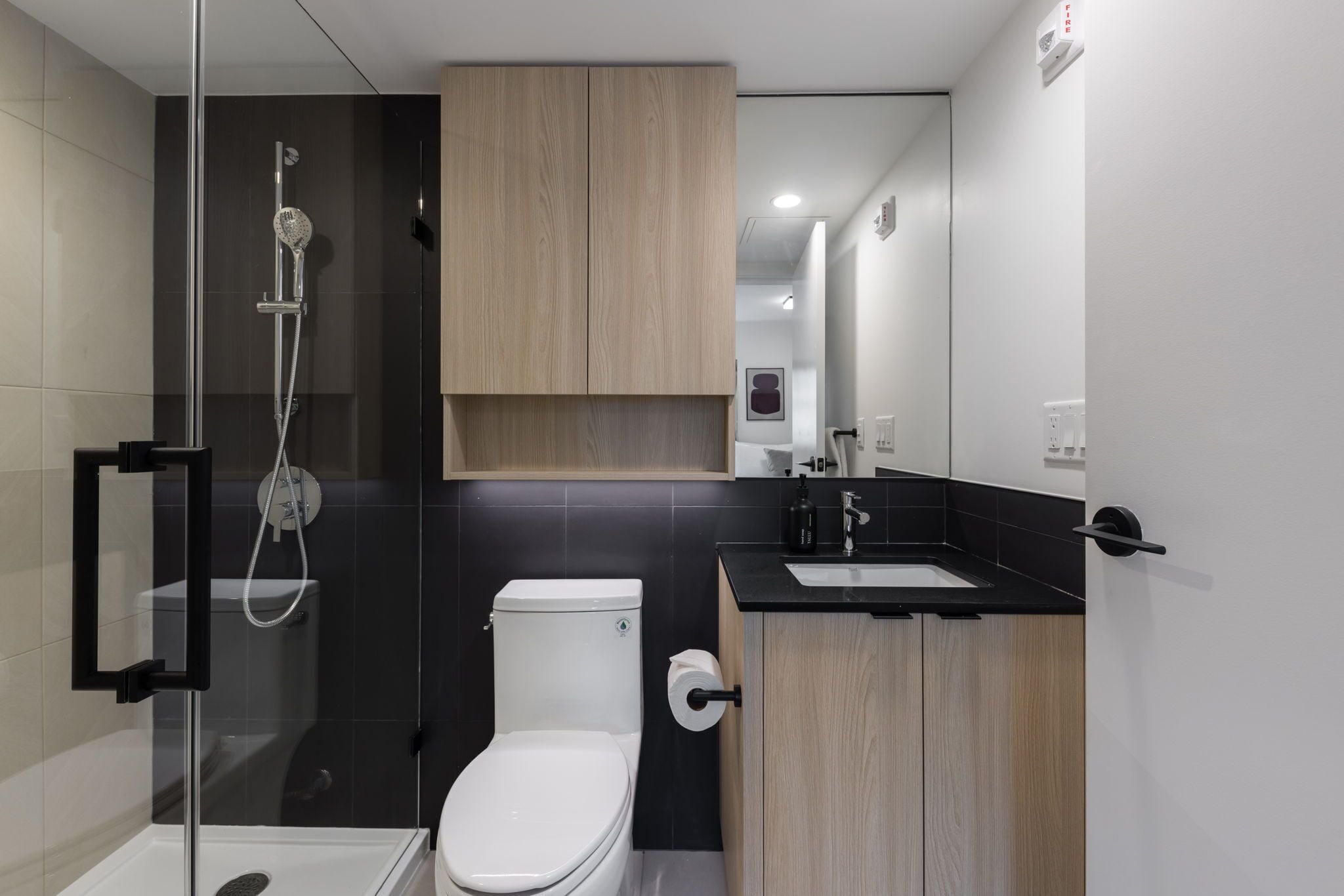 Un baño moderno con ducha envuelta en vidrio, inodoro y muebles de madera.