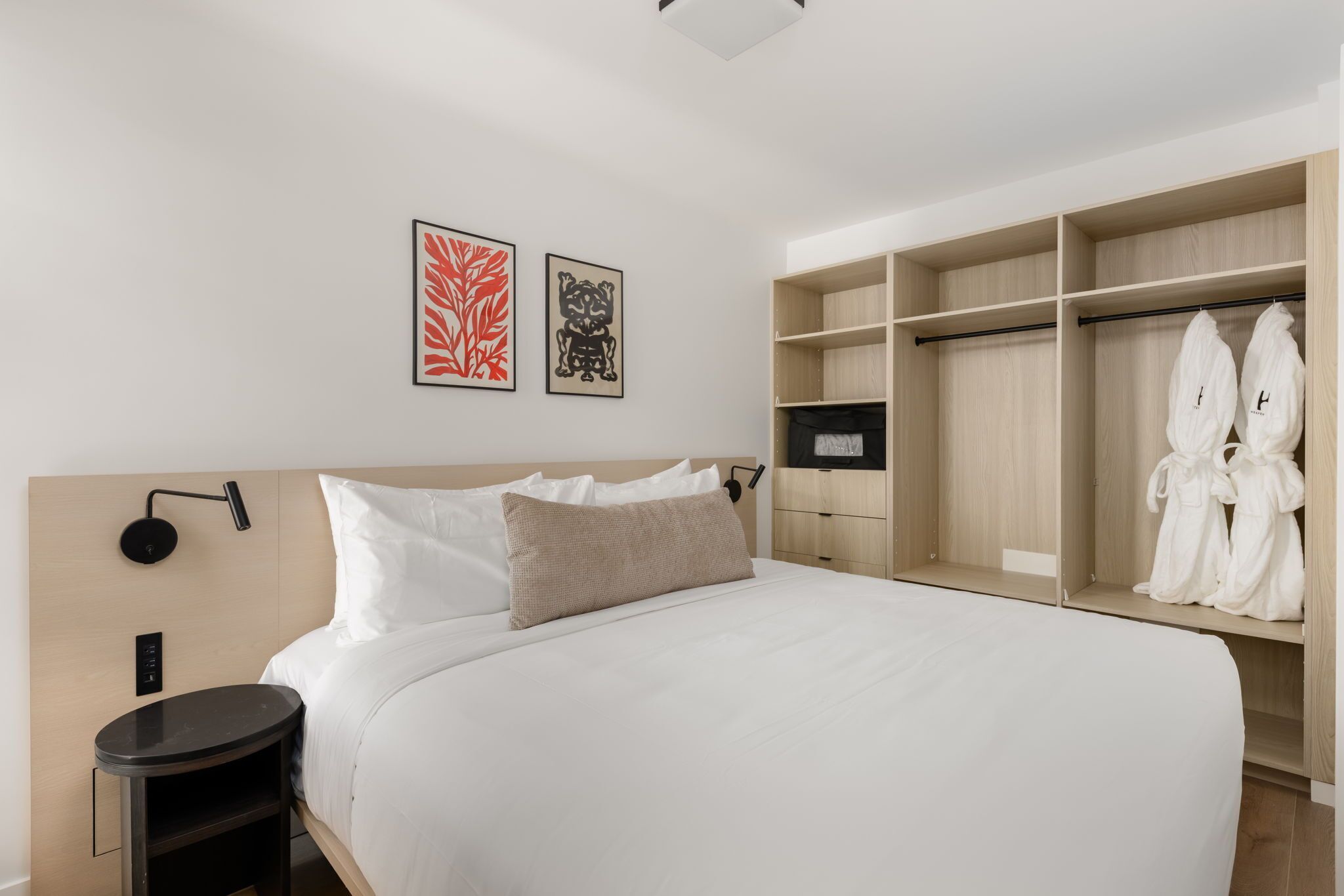 Une chambre d’hôtel moderne avec un grand lit, une armoire en bois et deux œuvres d’art accrochées au mur.
