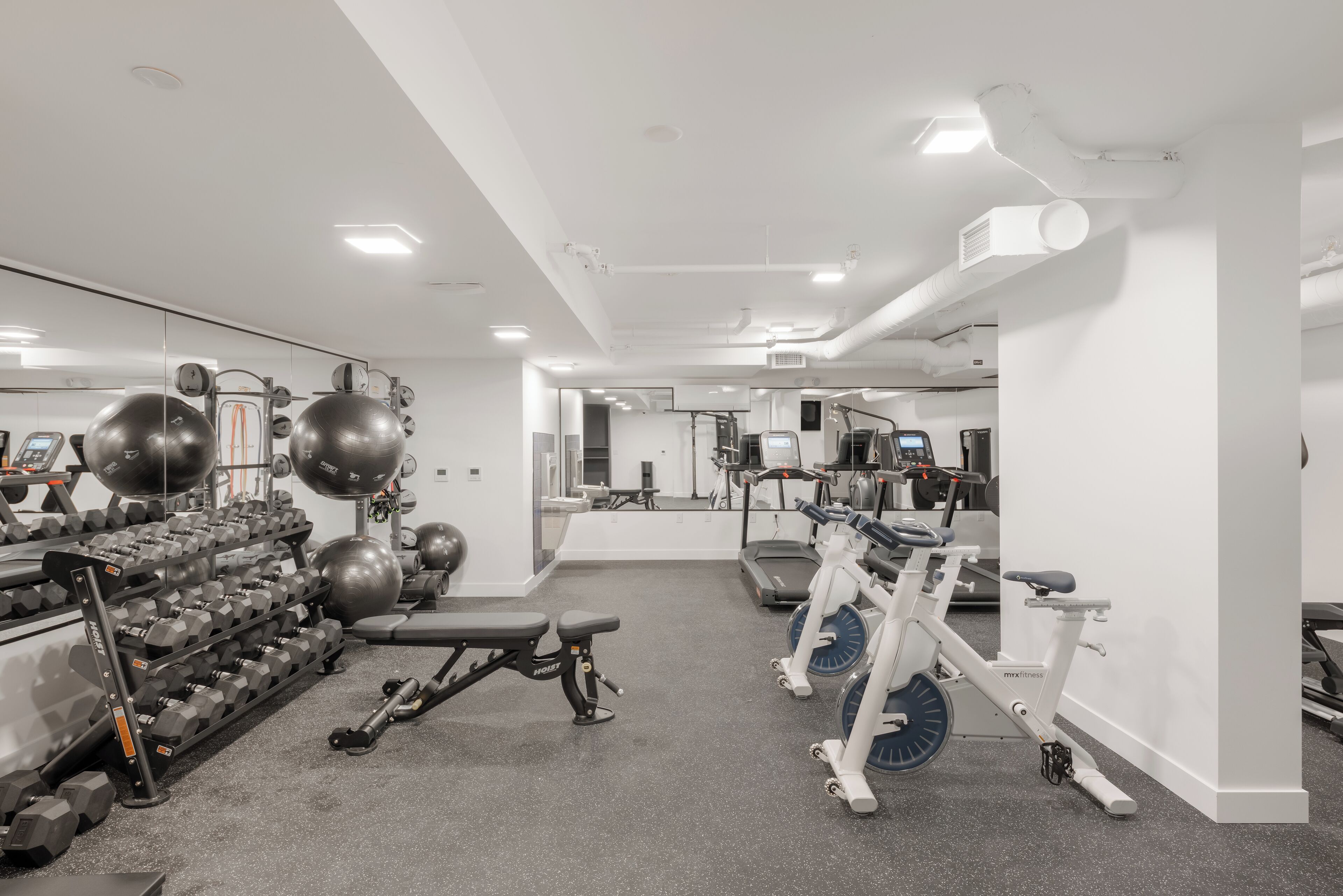 A gym with various exercise equipment, including dumbbells, a bench, and cardio machines.