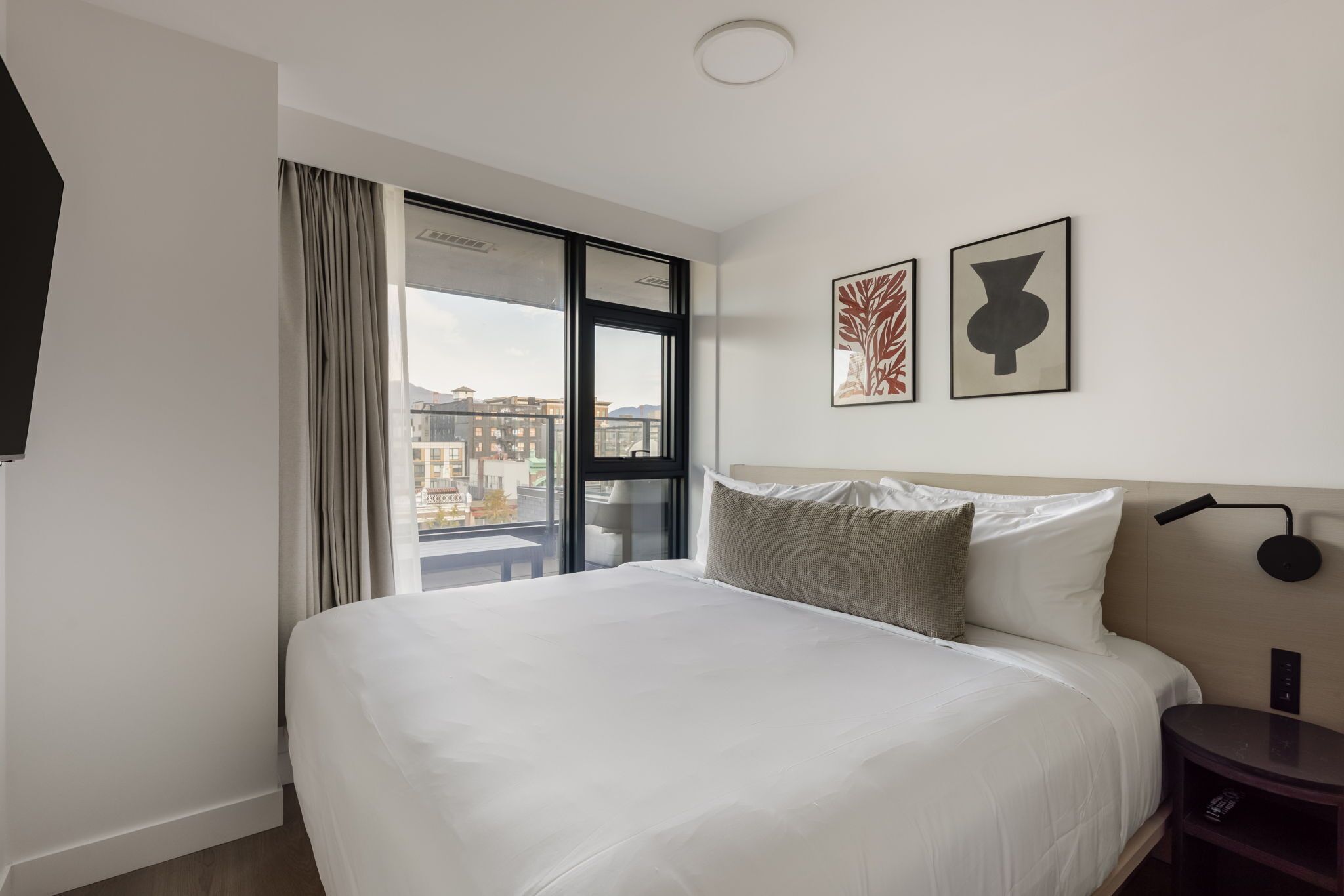 Ein Hotelzimmer mit einem großen Bett, Blick durch eine Schiebetür und zwei gerahmten Kunstwerken an der Wand.