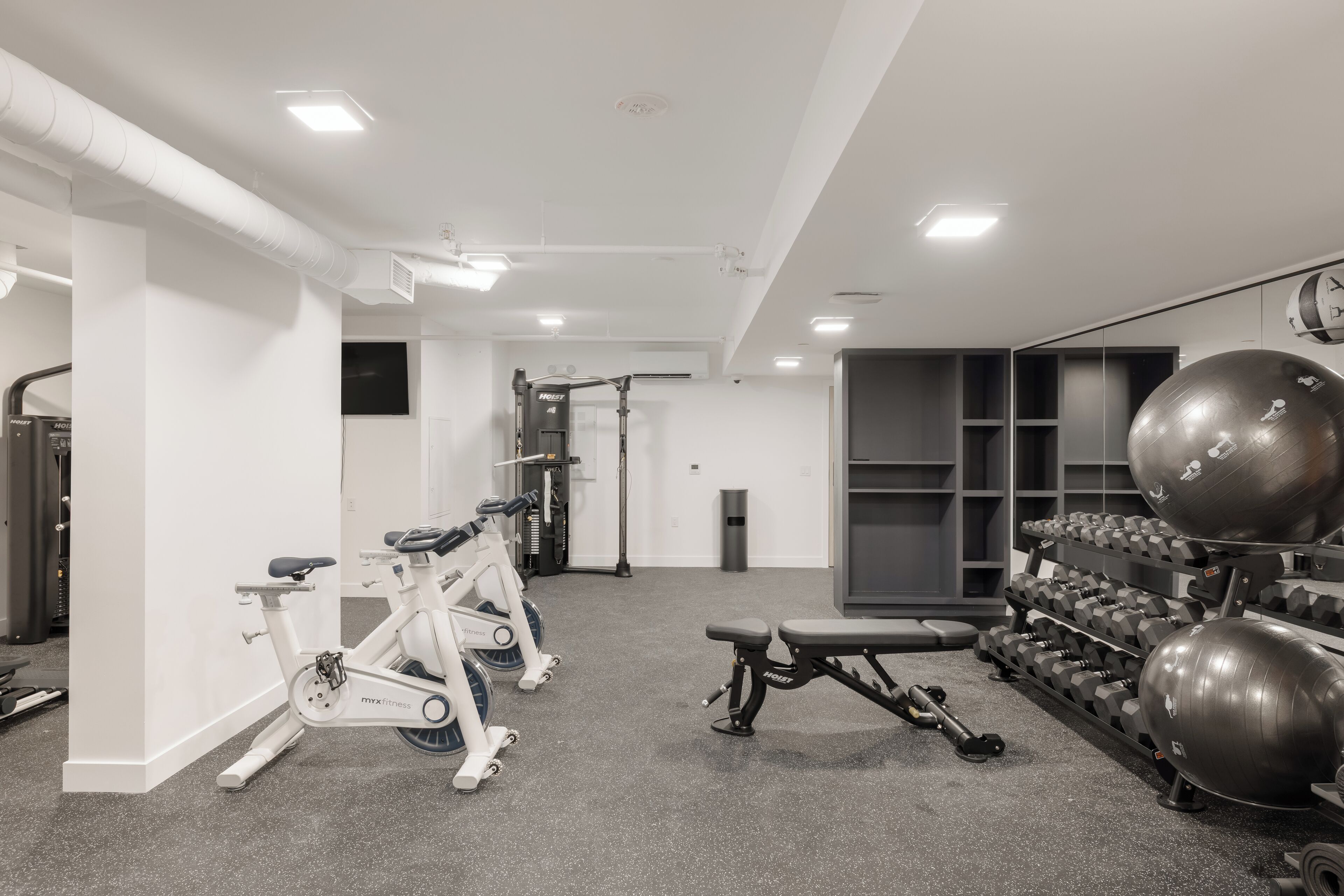 A gym with stationary bikes, a bench, dumbbells, and exercise balls.