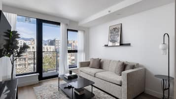 A modern living room with a sofa, coffee table, and a large window offering a city view.