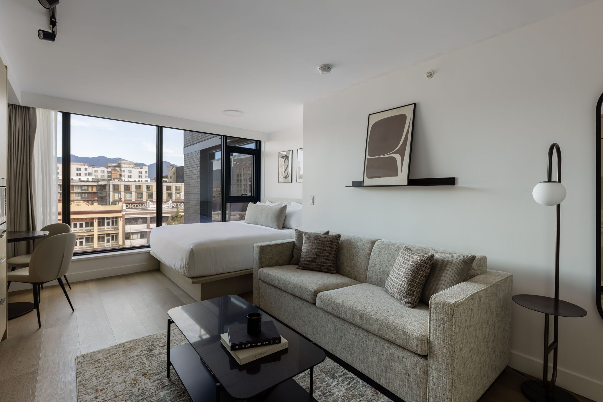 A modern hotel room with a large bed, a sofa, a desk, and a view of the cityscape.