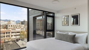 A modern hotel room with a large bed, a view of the cityscape through floor-to-ceiling windows, and two framed artworks on the wall. - Keefer House (Vancouver)