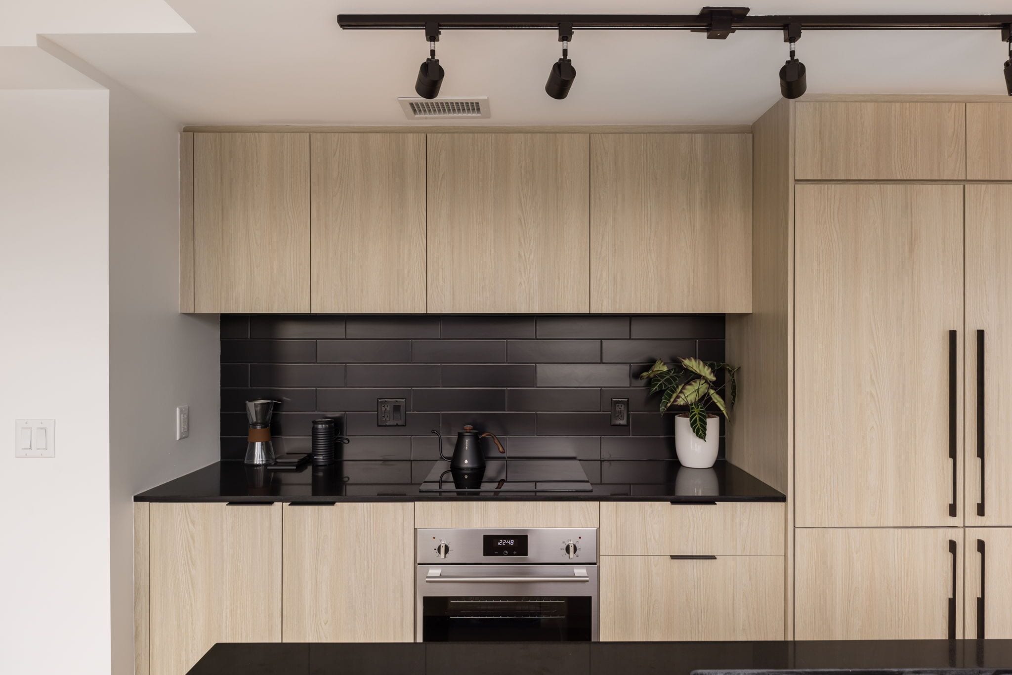 Eine moderne Küche mit hellen Holzschränken, einer schwarzen Arbeitsplatte und einem eingebauten Backofen.