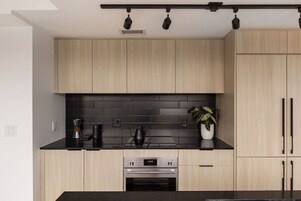 Una cocina moderna con armarios de madera clara, encimera negra y horno empotrado.