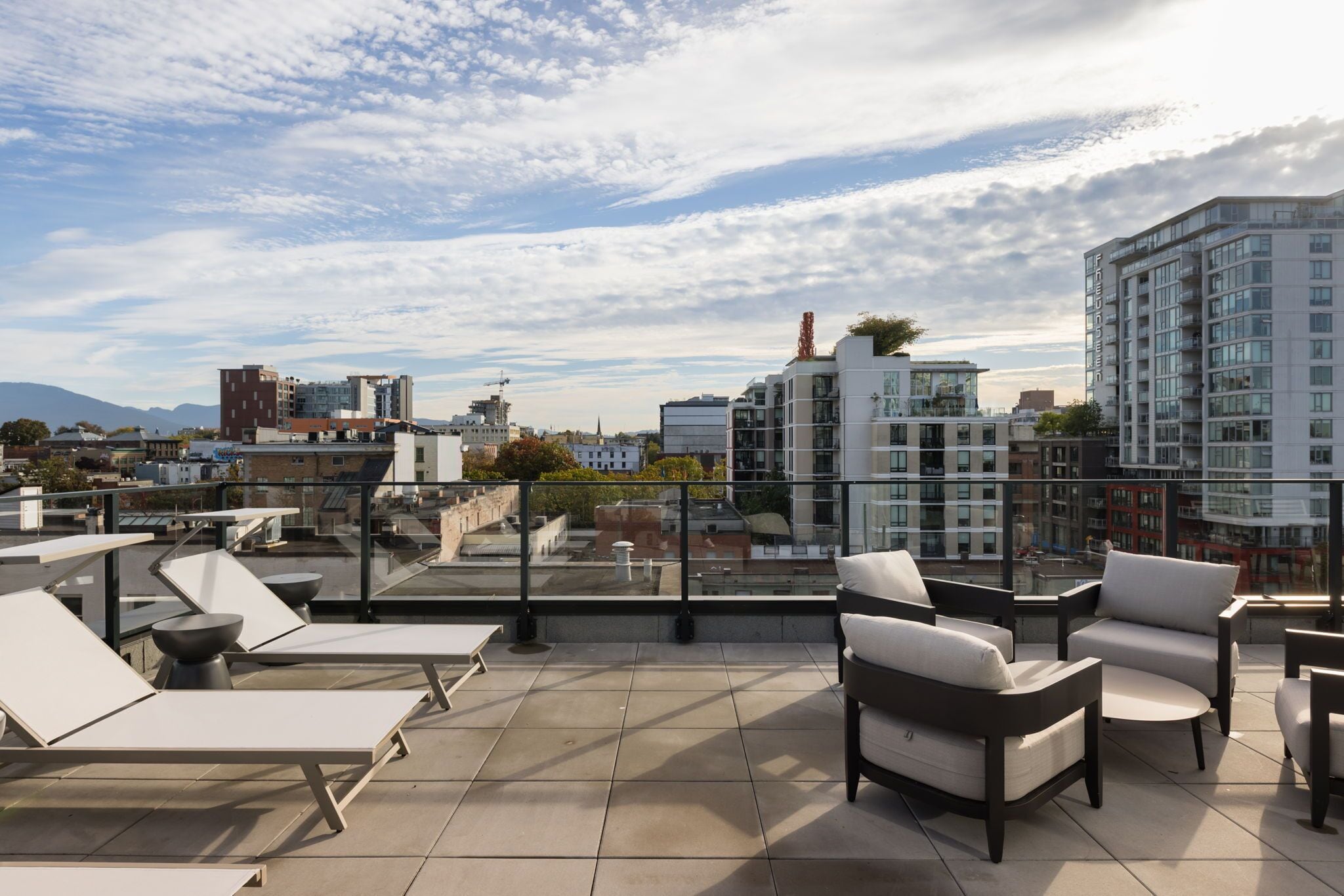 A rooftop terrace with sun loungers and chairs, offering a city view.