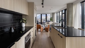 A modern kitchen with a black countertop, wooden cabinets, and a view of the city through large windows. - Keefer House (Vancouver)