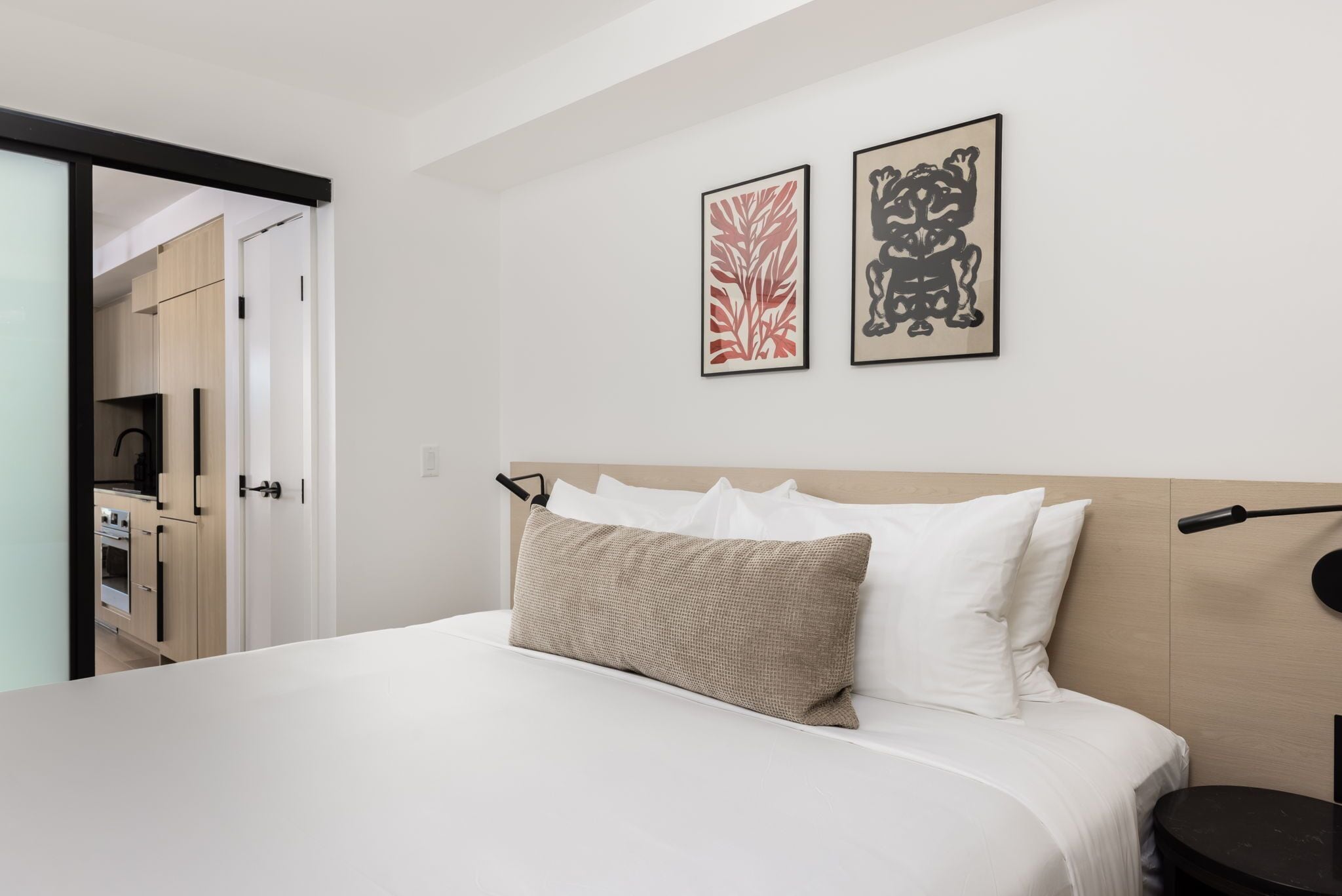 Quarto com cama, mesa de cabeceira, luminária na parede e duas obras de arte emolduradas.