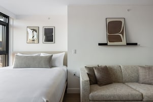 Una habitación de hotel con una cama, un sofá y dos cuadros enmarcados en la pared.