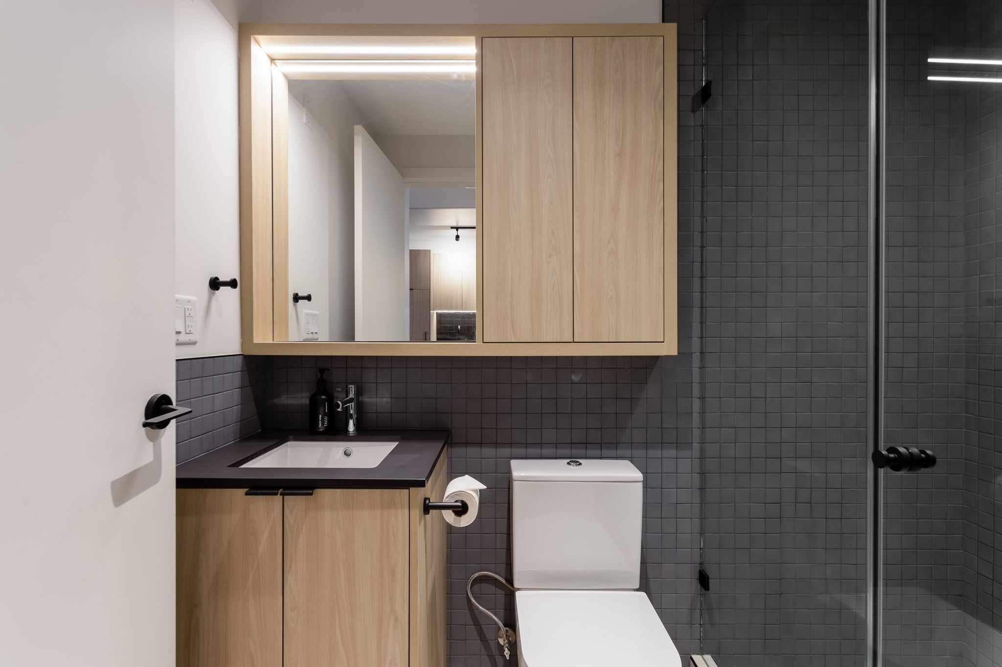 A modern bathroom with a wooden vanity, a toilet, and a glass shower enclosure.