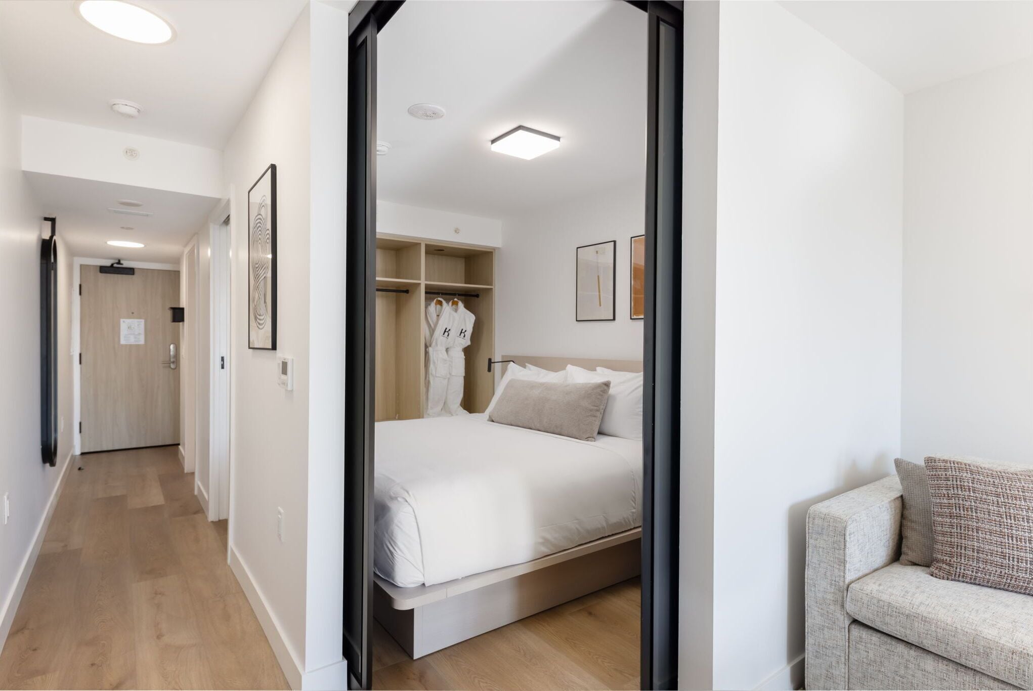 Une chambre d’hôtel comprenant un lit, une armoire, un coin salon et un couloir.