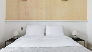 A neatly made bed with white linens, two bedside lamps, and a wall-mounted light fixture. - Blueground | Grands Blvds, washer, nr shops (Paris)