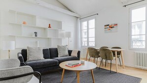 A modern living room with a sofa, armchairs, a coffee table, and a dining area with chairs and a table. - Blueground | Grands Blvds, washer, nr shops (Paris)