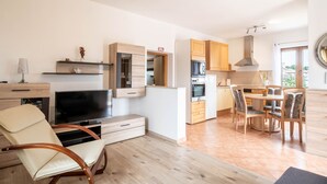 A modern kitchen with wooden cabinets, a dining area with a table and chairs, and a TV in the living area.