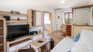 A modern room with a flat-screen TV, wooden furniture, a dining area, and a large window.