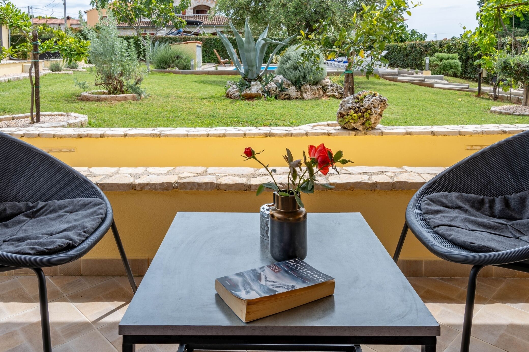 Un patio con una mesa, dos sillas, un libro y un florero con flores.