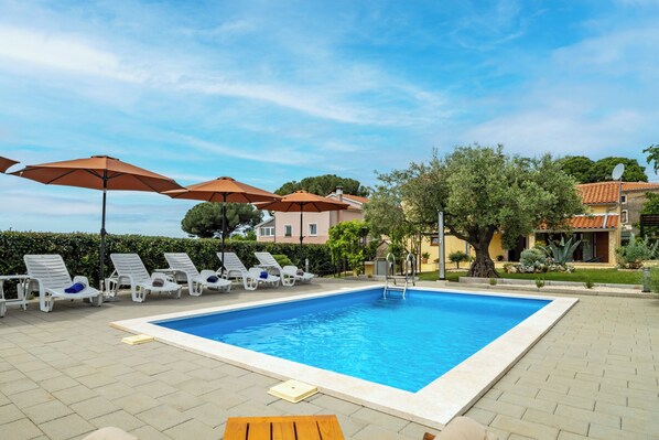 A rectangular swimming pool with a tiled deck, surrounded by white lounge chairs and orange umbrellas. - Villa Olea (Istria - Kaštelir) (Kaštelir)