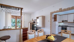 A modern kitchen with white cabinets, a wooden dining table, and a fruit bowl.