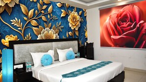 Ein modernes Hotelzimmer mit einem großen Bett, einem Nachttisch mit Telefon und Wasserflaschen sowie einer Wand mit floralem Dekor.