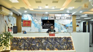 Ein Hotelrezeptionsschalter mit Marmor-Wandverzierungen, einem digitalen Display und einer Topfpflanze.