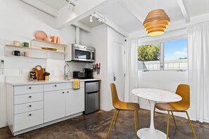 A modern kitchen with white cabinetry, a built-in microwave, and a stainless steel refrigerator. There is a dining area with a white table and two chairs.