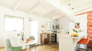 A bright kitchen with white walls, a wooden cabinet, a microwave, and a sink. There is a dining table with chairs and a vase with flowers. - 2 Rooms, Sleeps 8 | Retro Hotel w/ Pool | Wesley King Studio Buyout by AvantStay (Palm Springs)