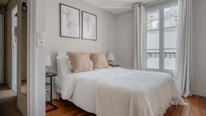 A bedroom with a large bed, two bedside lamps, and a window with curtains. - Blueground | Ternes, near shops, dining (Paris)