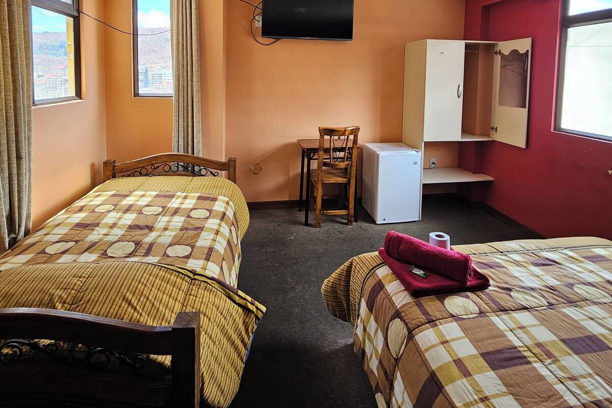 A hotel room with two beds, a desk, a chair, a television, and a wardrobe.