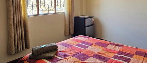A room with a bed, a window with curtains, and a small heater.