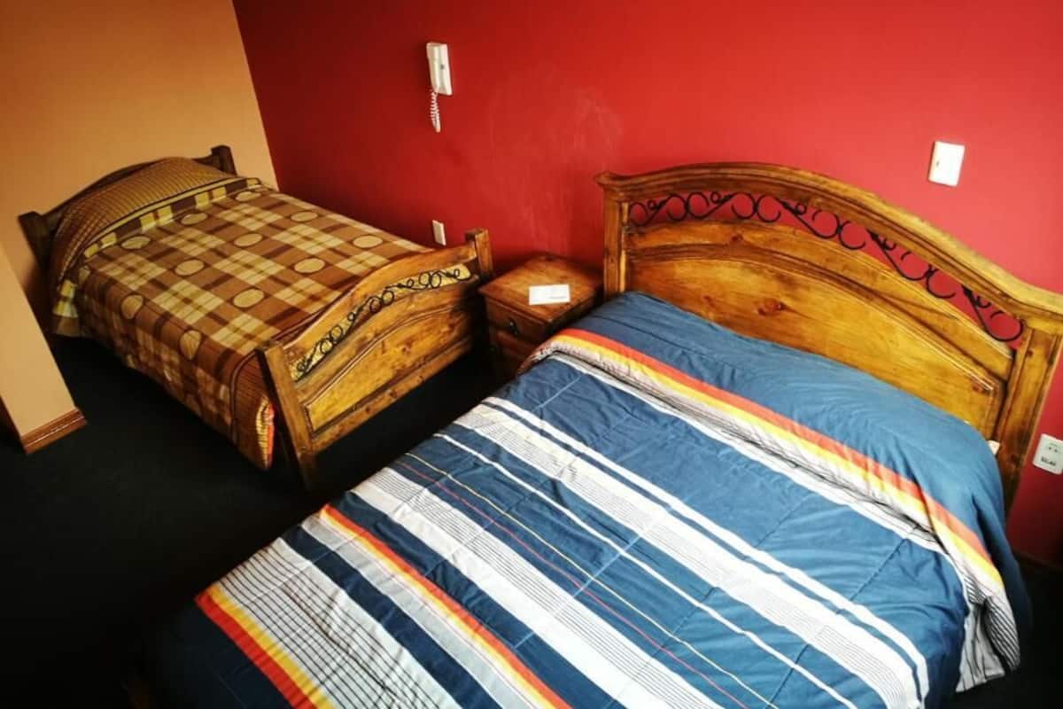 A room with two beds, one with a checkered bedspread and the other with a striped bedspread.