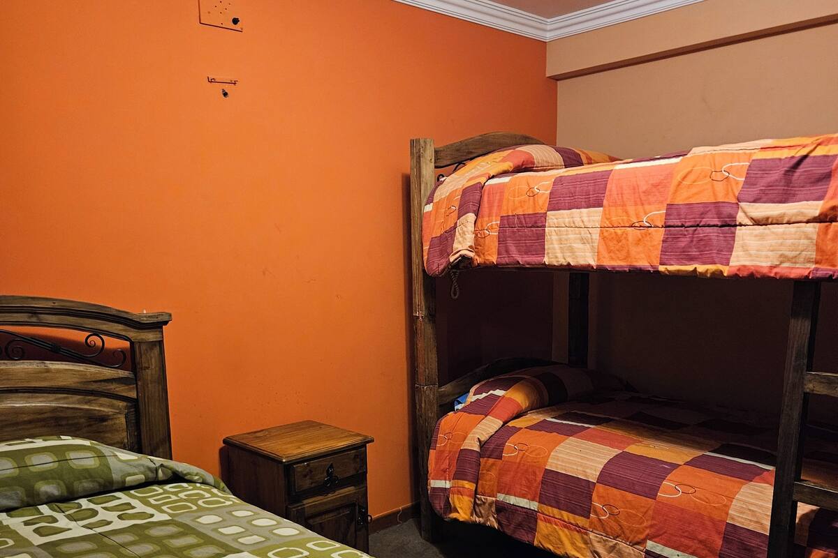 A room with two beds, one with a checkered quilt and the other with a geometric pattern. There is a small wooden nightstand between the beds.