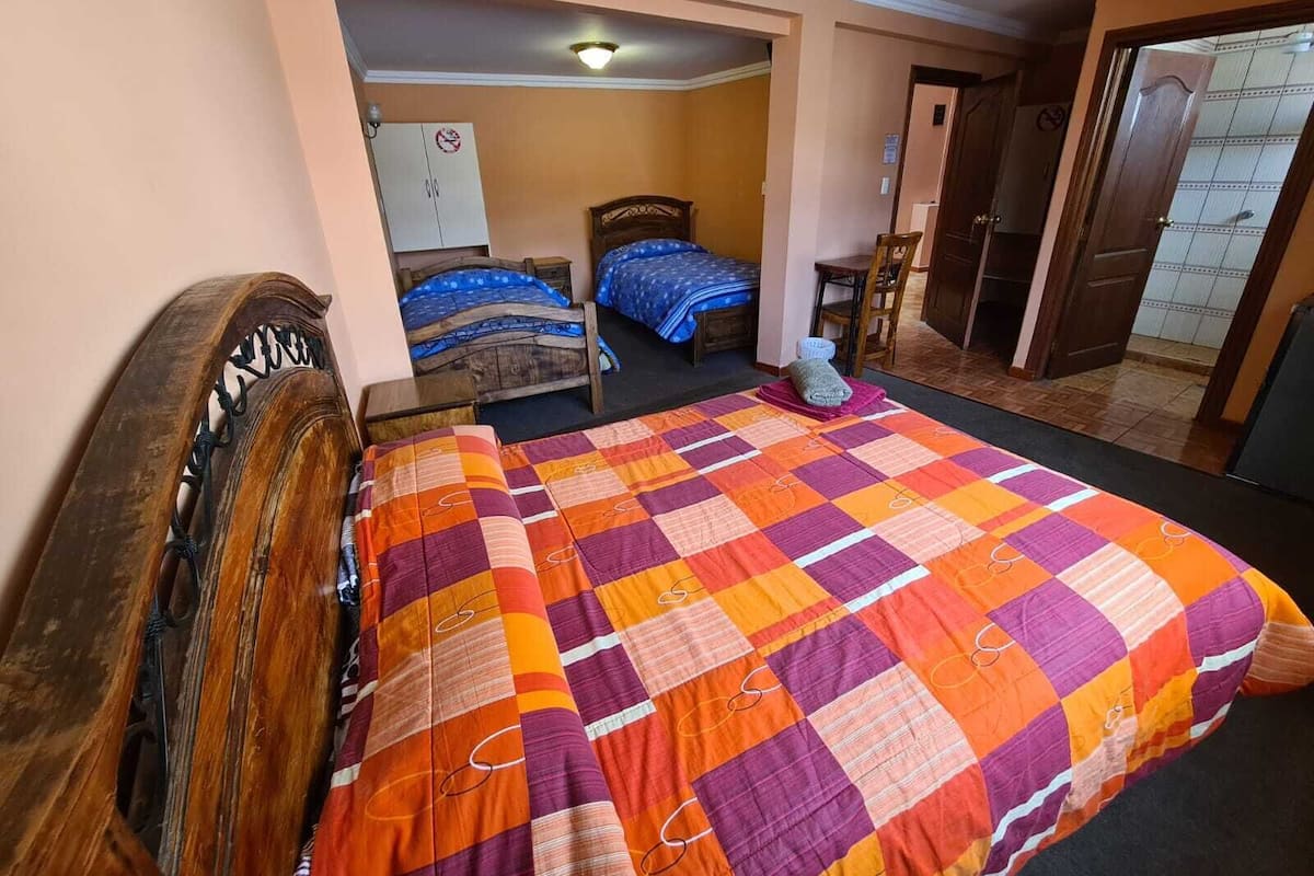A bedroom with two beds, a wooden headboard, a colorful quilt, and a chair.