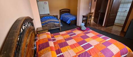 A bedroom with two beds, a wooden headboard, a colorful quilt, and a chair.